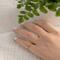Hand wearing 14K yellow gold birthstone stackable rings with 2mm round stones sizes 4-10 on a white fabric with green plant in background  
